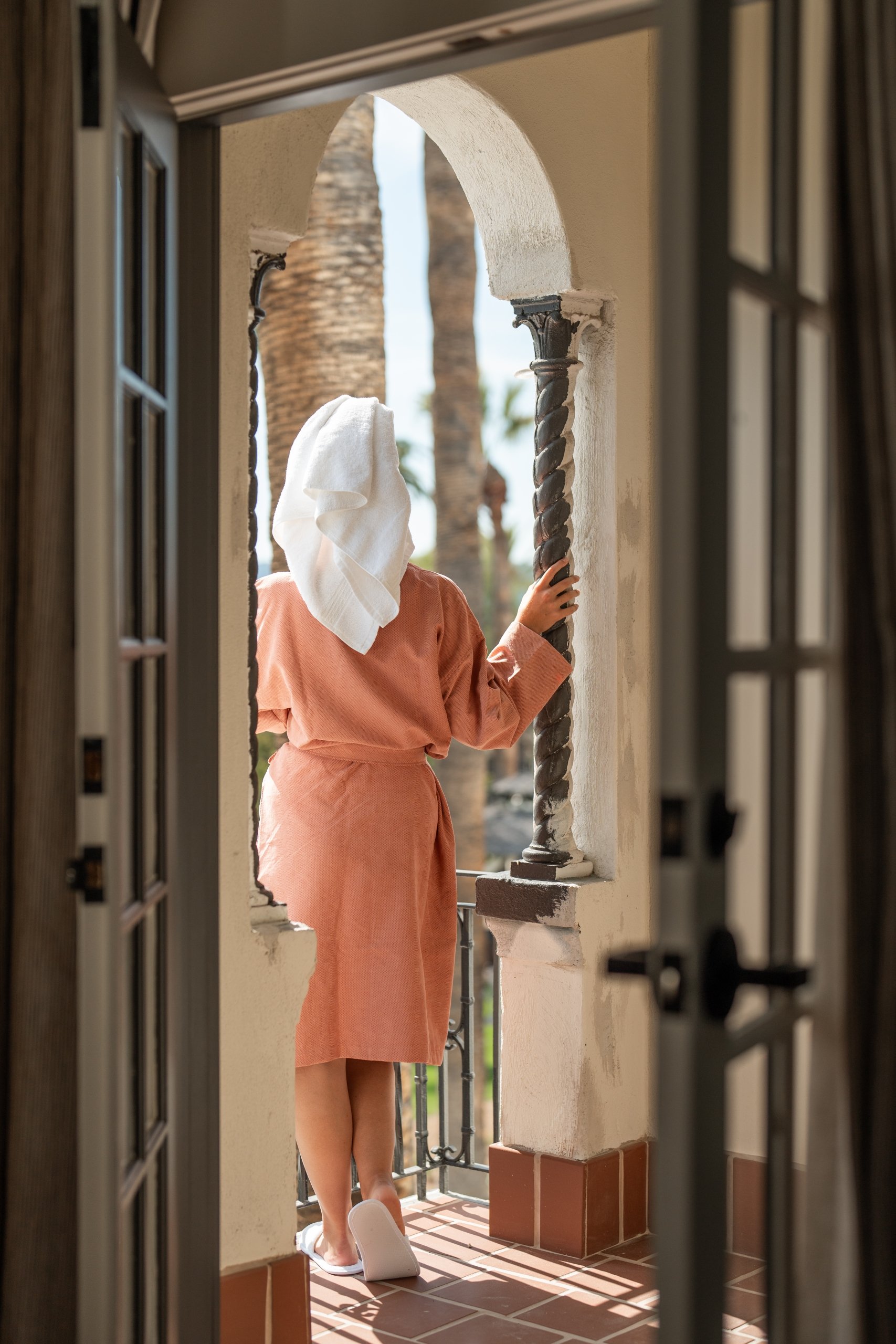 Woman in a robe and hair towel looking outside from her room.